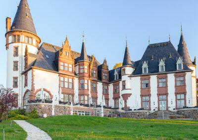 Frontaufnahme des Hotels mit Türmen und Rasen vor dem Eingang.